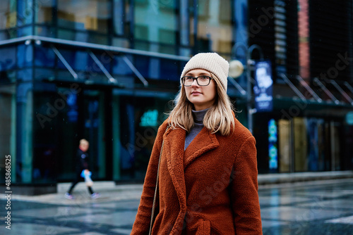 Woman in coat and eyeglasses walking at city street at rainy day