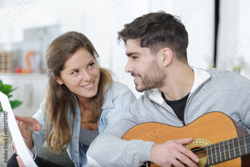 woman holding sheetmusic for man playing guitar