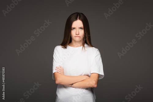 offended woman in white t-shirt standing with crossed arms isolated on dark grey