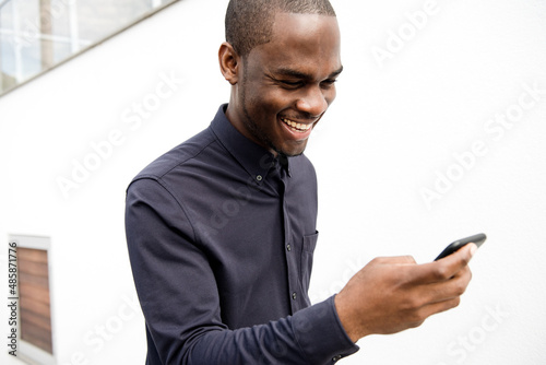 African American man laughing and looking at cellphone by white wall