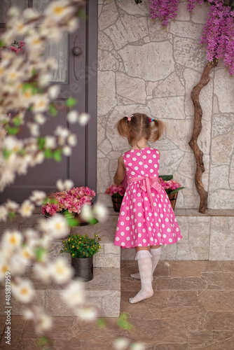 a little girl in pink dress with white polka dots standing on porch © Анна Минина