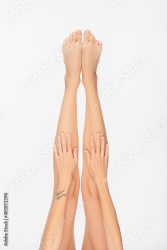 partial view of young woman with tattooed arm and slender legs isolated on white