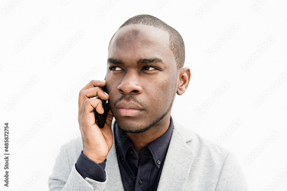 Close up African American business man talking with cellphone by isolated white wall Close up African American business man talking with cellphone by isolated white wall