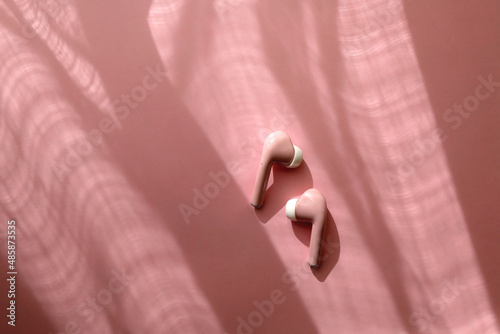 Pink wireless bluetooth earphones on pink background. Flat lay.