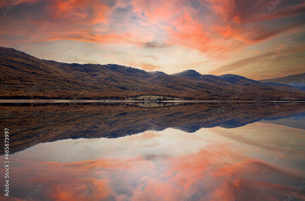landscape of mountains and lake with orange sky reflected in the water