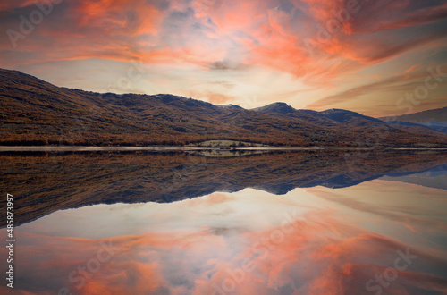 landscape of mountains and lake with orange sky reflected in the water