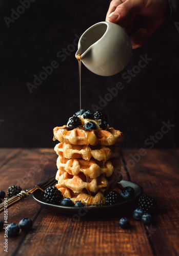 Maple syrup being poured over stack of belgian waffles with berries. photo