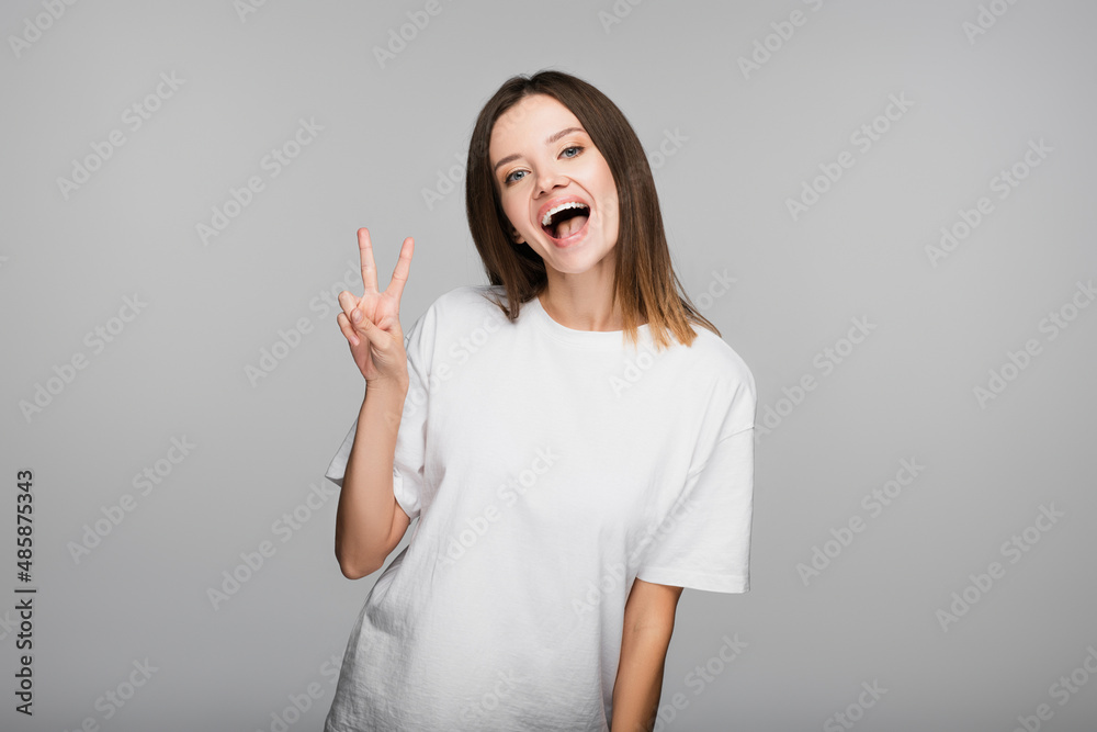 thrilled woman in white t-shirt showing victory sign while looking at camera isolated on grey thrilled woman in white t-shirt showing victory sign while looking at camera isolated on grey