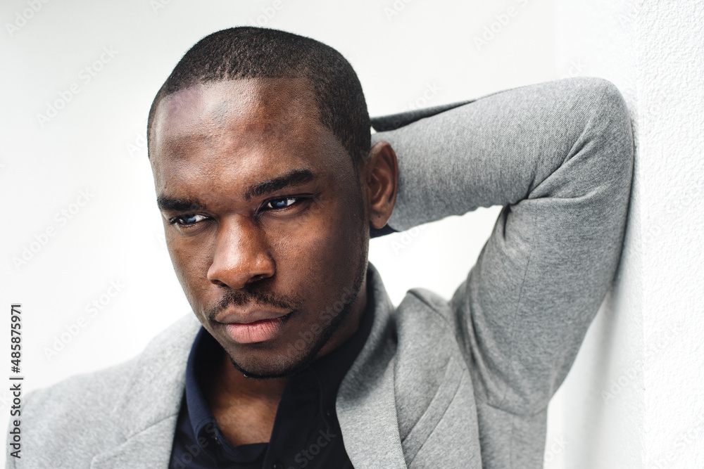 Obraz premium Close up handsome african american man leaning against wall with hand behind head and looking away