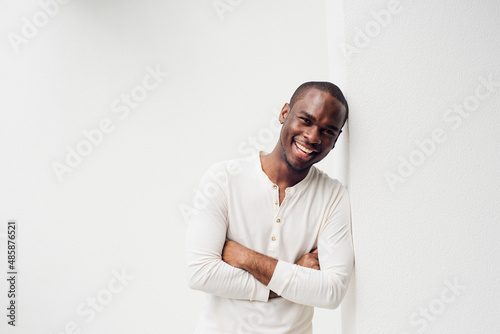handsome smiling african american man leaning against wall with arms crossed