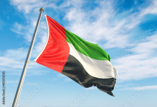 United Arab Emirates flag waving in the wind on flagpole. United Arab Emirates flag waving a blue cloudy sky photo