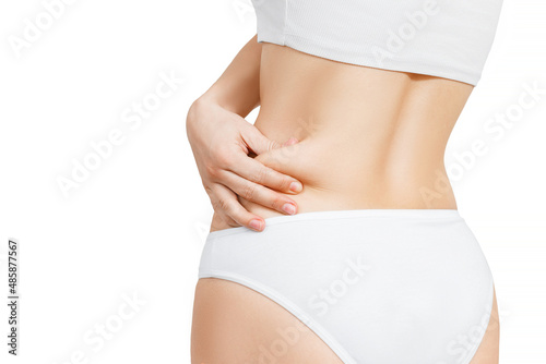 woman in white underwear shows extra fat on the sides of her stomach with her hand. isolate on white background.