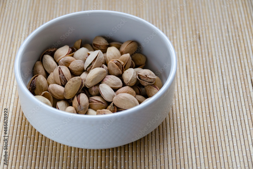 Roasted salted pistachios in a basket, plate on a white background Roasted salted pistachios in a basket, plate on a white background