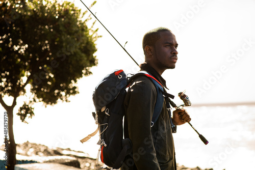 african American man standing outside with fishing rod and bag
