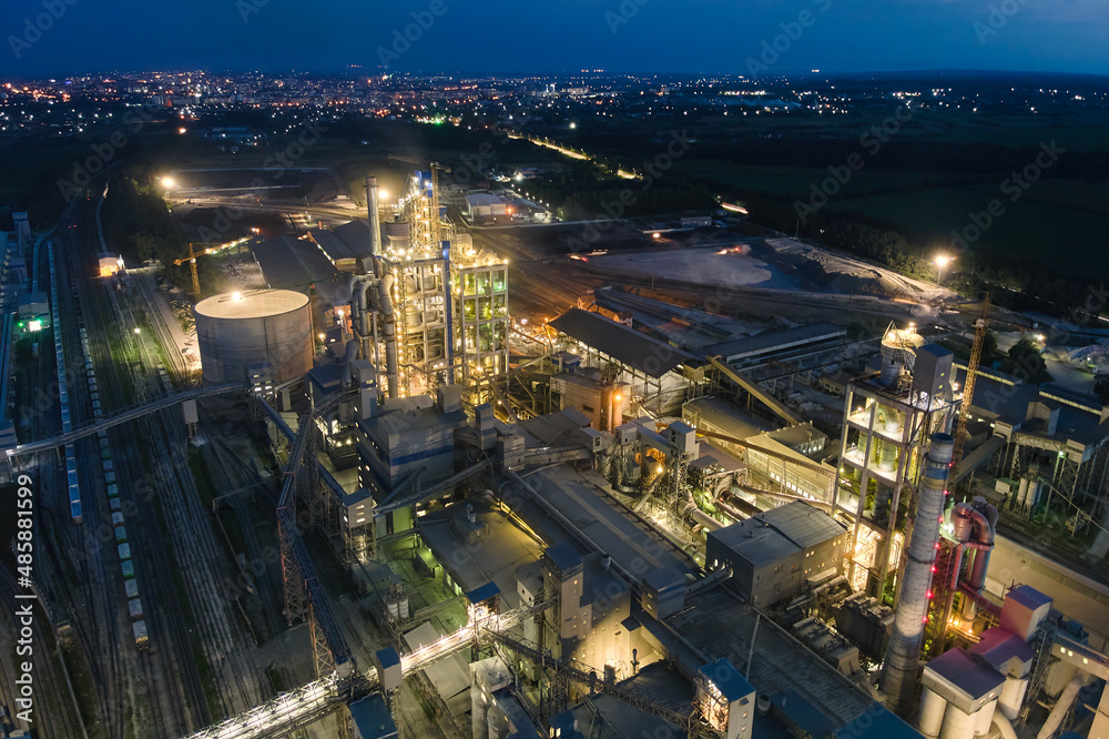 Aerial view of cement factory with high concrete plant structure and tower cranes at industrial production area at night. Manufacture and global industry concept