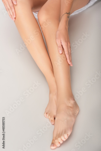 cropped view of barefoot woman touching smooth legs while sitting on white background