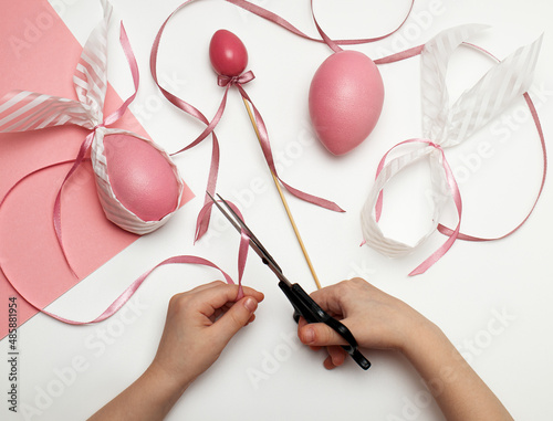 Children's hands hold scissors and pink ribbons. Easter decoration. Preparation for the Happy Easter holiday