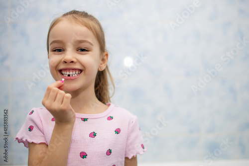 Girl child shows her mouth without one lost milk tooth and smiles. A child in the bathroom holds a milk tooth in his hand and smiles. Free space for text