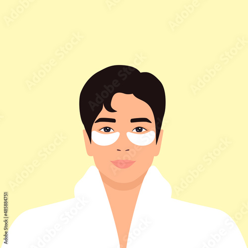 Young asian man in a white bathrobe with white eye patches on his face. Daily skincare routine