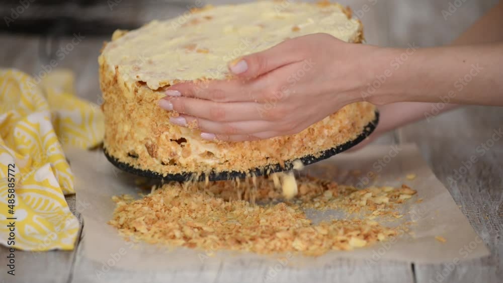 A woman decorates a cake smeared with cream with biscuit crumbs. A woman decorates a cake smeared with cream with biscuit crumbs.