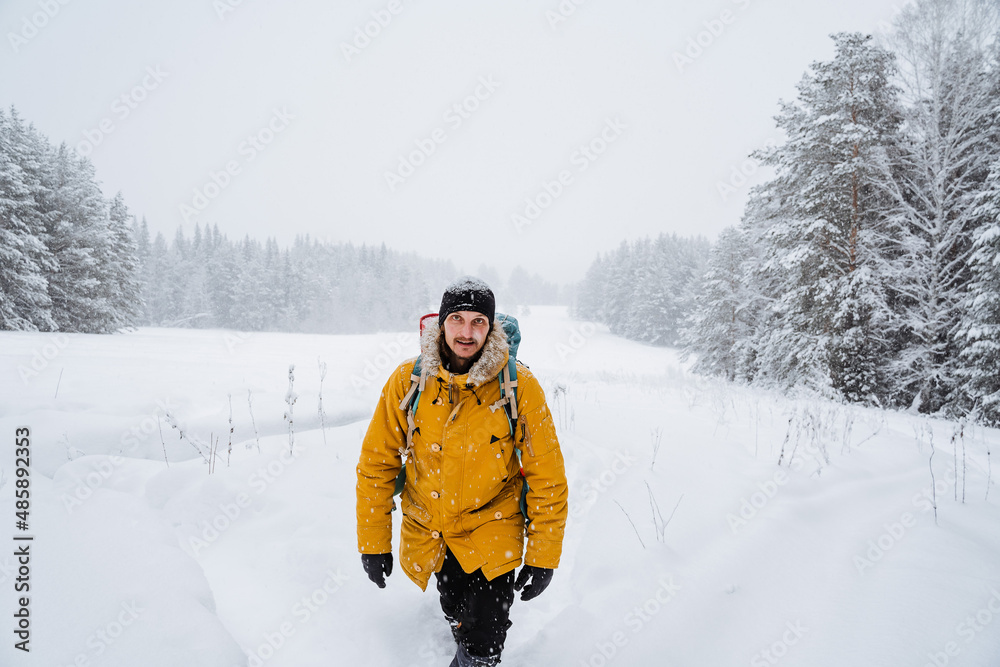 Charming traveler walking with hiking backpack in the snowy woods. Bright backpack with equipment. Climbing the mountain in winter. Survival in the wild.