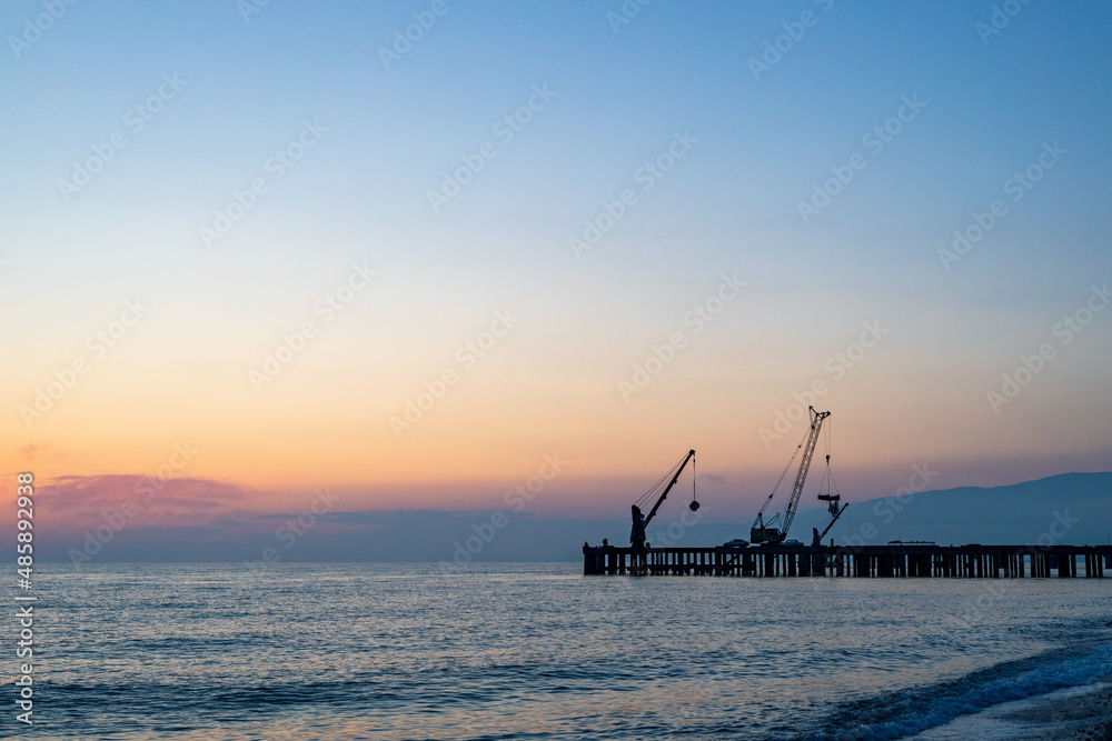 silhouette of cranes on the old pier, sea and mechanisms for loading ships
