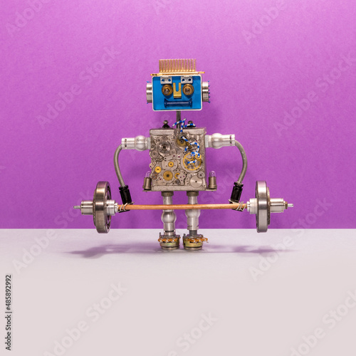 A toy robot weightlifter lifts a heavy steel barbell. strength weight training exercise. Sport fitness, weightlifting and power lifting athletics workouts. Violet gray background, copy space