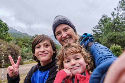 A happy family taking a selfie portrait with smartphone in the mountains in winter