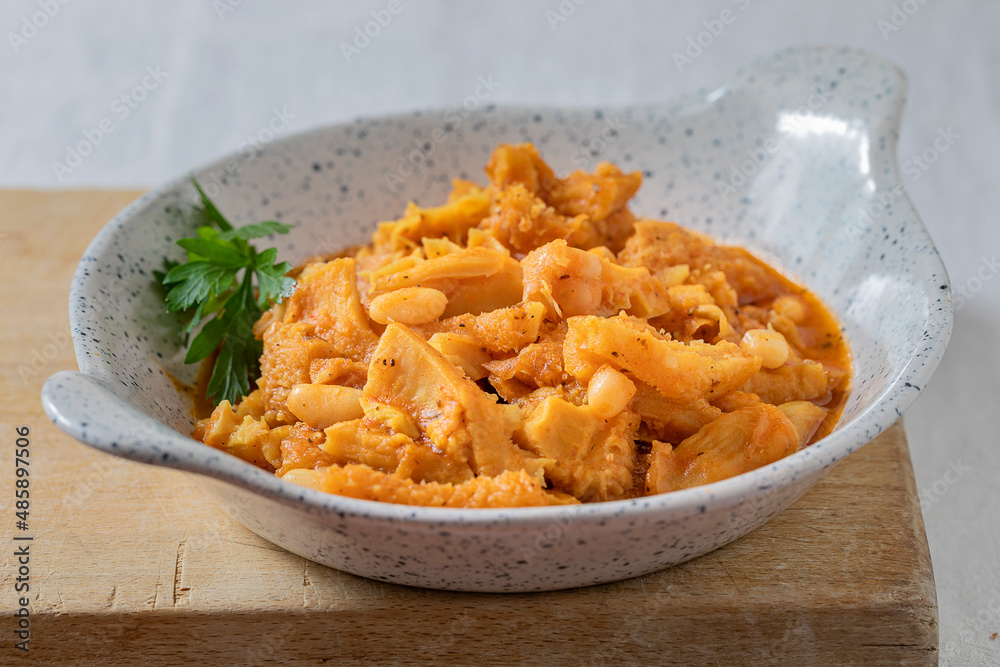 Small bowl with tomato tripe with beans on a wooden cutboard.