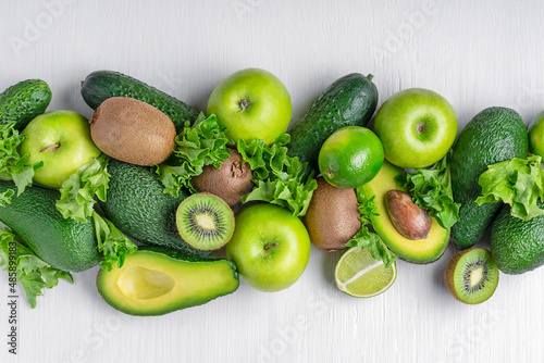 Different green fruits and vegetables whole and sliced such as avocado, apple, lime, kiwi, lettuce and cucumber laying on white wooden background used as ingredients for healthy eating and vegan diet