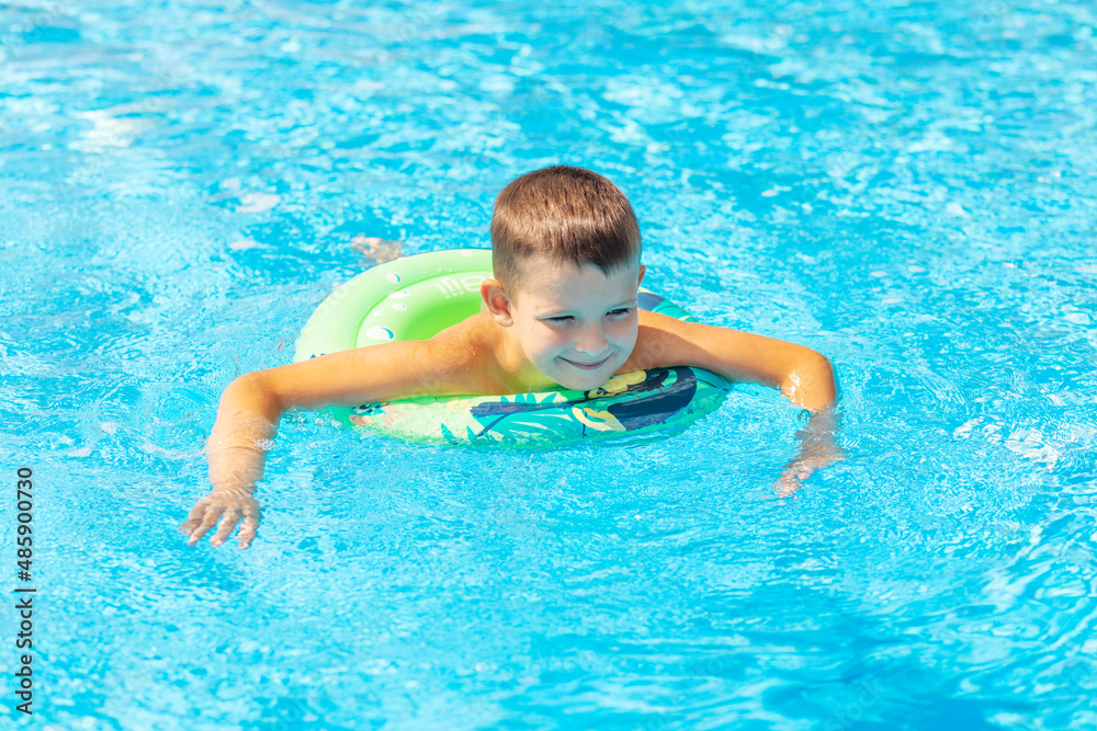 Funny happy child boy in swiming pool on inflatable rubber circle ring. Kid playing in pool. Summer holidays and vacation concept