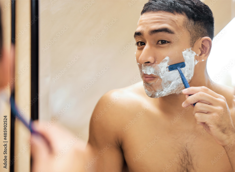 Lets put this razor to the test. Shot of a young man looking in the mirror while shaving his beard.