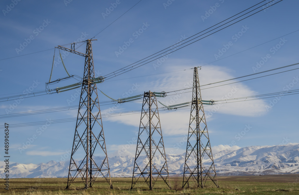 Metal poles of a high-voltage line against the backdrop of snow-capped mountains