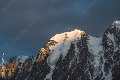 Awesome scenery with sunlit snow mountains in cloudy sky at sunrise. Dark scenic landscape with large glacier in sunrise colors. © sablinstanislav