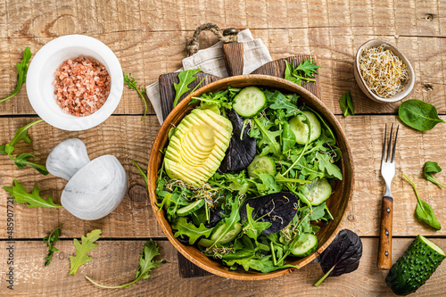 Green vegan salad with green leaves mix, avocado and vegetables. Wooden background. Top view