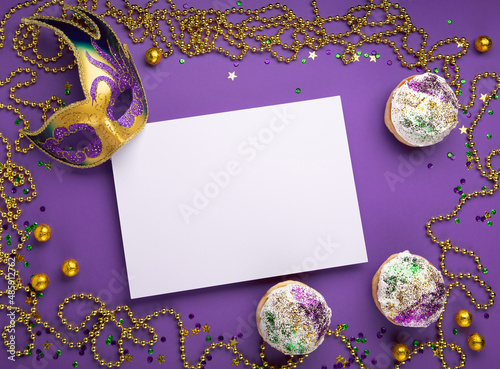 Fotografie Mardi Gras King Cake sufganiyot donuts, masquerade festival carnival mask, gold beads and golden, green, purple confetti on purple background