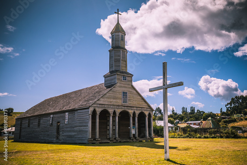 Schicke Holzkirche Aldachildo auf Chiloe mit heller Holz Fassade und einem riesigen hölzernen Kreuz auf dem grünen Rasen photo