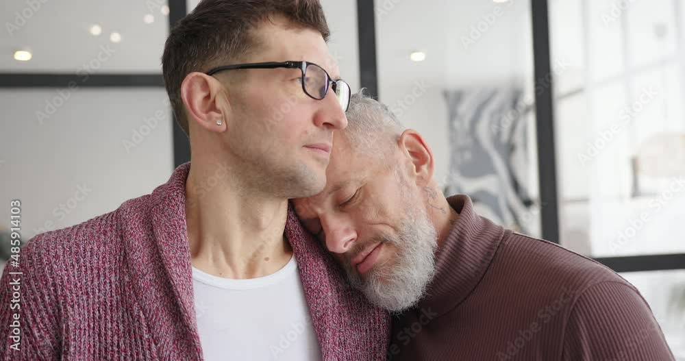 Gay LGBT man puts head on shoulder of partner hugging at home