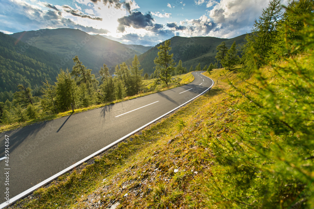 Fototapeta premium Motorbiker riding in Austrian Alps in beautiful sunset dramatic sky. Travel and freedom, outdoor activities