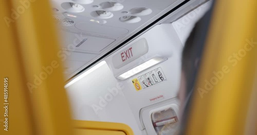 Handheld shot of exit sign above emergency door near wings, inside an airplane cabin during flight with turbulence. Interior, generic, travel.