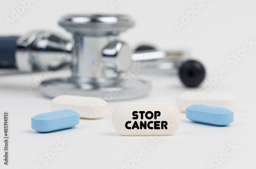 On a white surface lie pills, a stethoscope and a tablet with the inscription - STOP CANCER