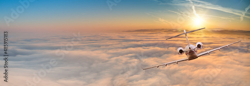 Private jet plane flying above clouds in beautiful sunset. Shot from back view