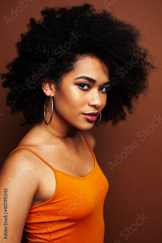 pretty young african american woman with curly hair posing cheerful gesturing on brown background, lifestyle people concept