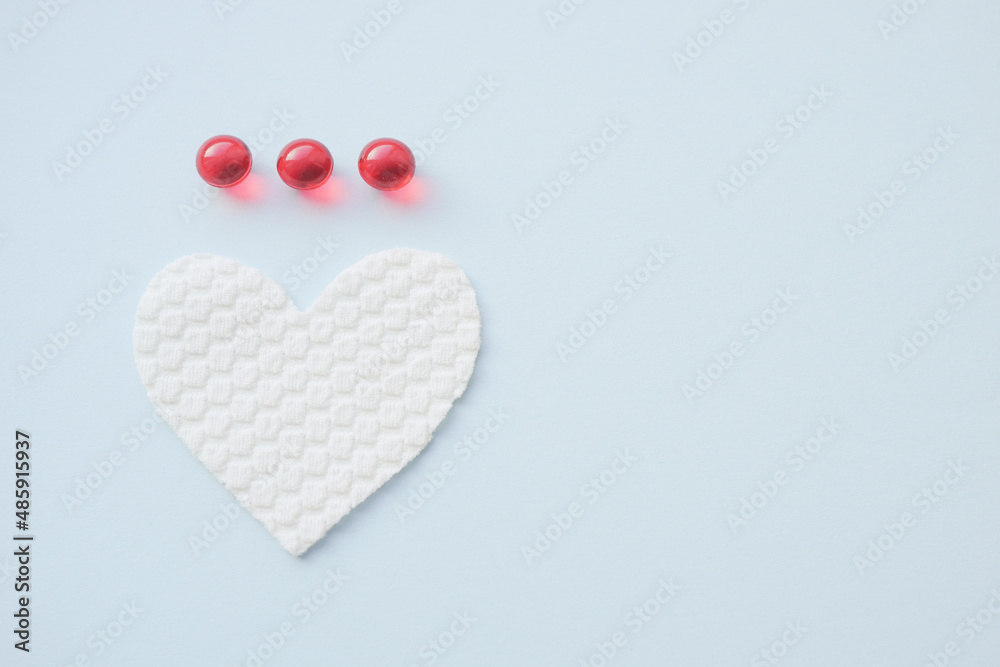 Fototapeta premium Three red vitamins and white heart on pale blue table. Copy space