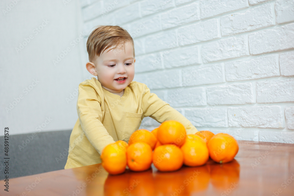 A little boy 2 years old holds tangerines in his hands. The kid wants to sit on citrus fruits for the first time. A little boy 2 years old holds tangerines in his hands. The kid wants to sit on citrus fruits for the first time.