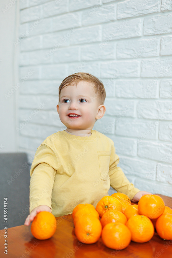 A little boy 2 years old holds tangerines in his hands. The kid wants to sit on citrus fruits for the first time. A little boy 2 years old holds tangerines in his hands. The kid wants to sit on citrus fruits for the first time.