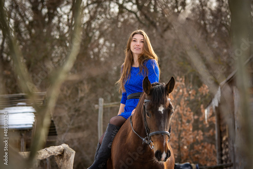 A girl in a blue dress sits on a horse against the backdrop of a winter forest