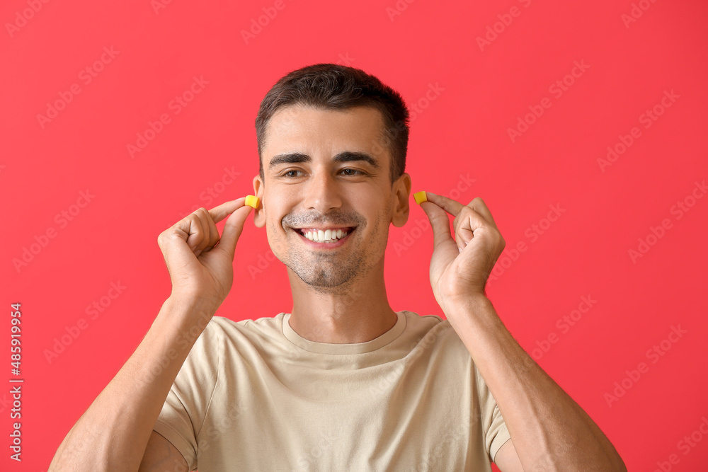 Smiling young man putting ear plugs on red background Smiling young man putting ear plugs on red background