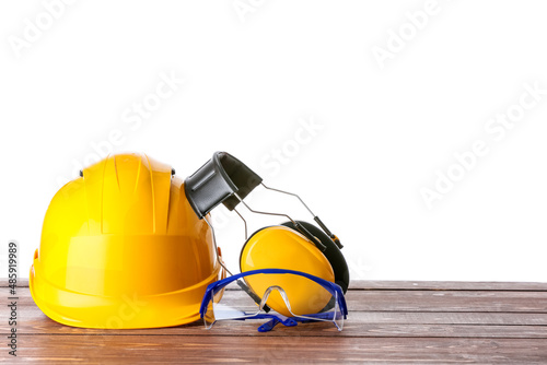 Safety hardhat and protective ear muffs with glasses on wooden table against white background