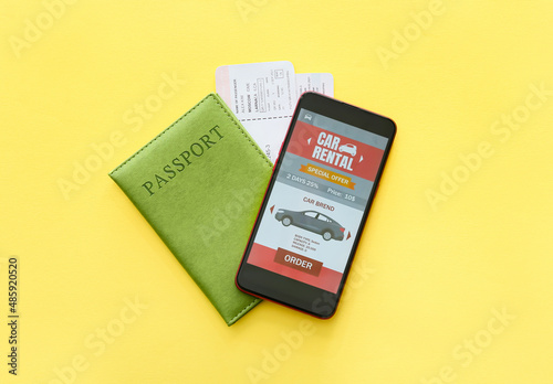 Mobile phone with open car rent app and passport on yellow background
